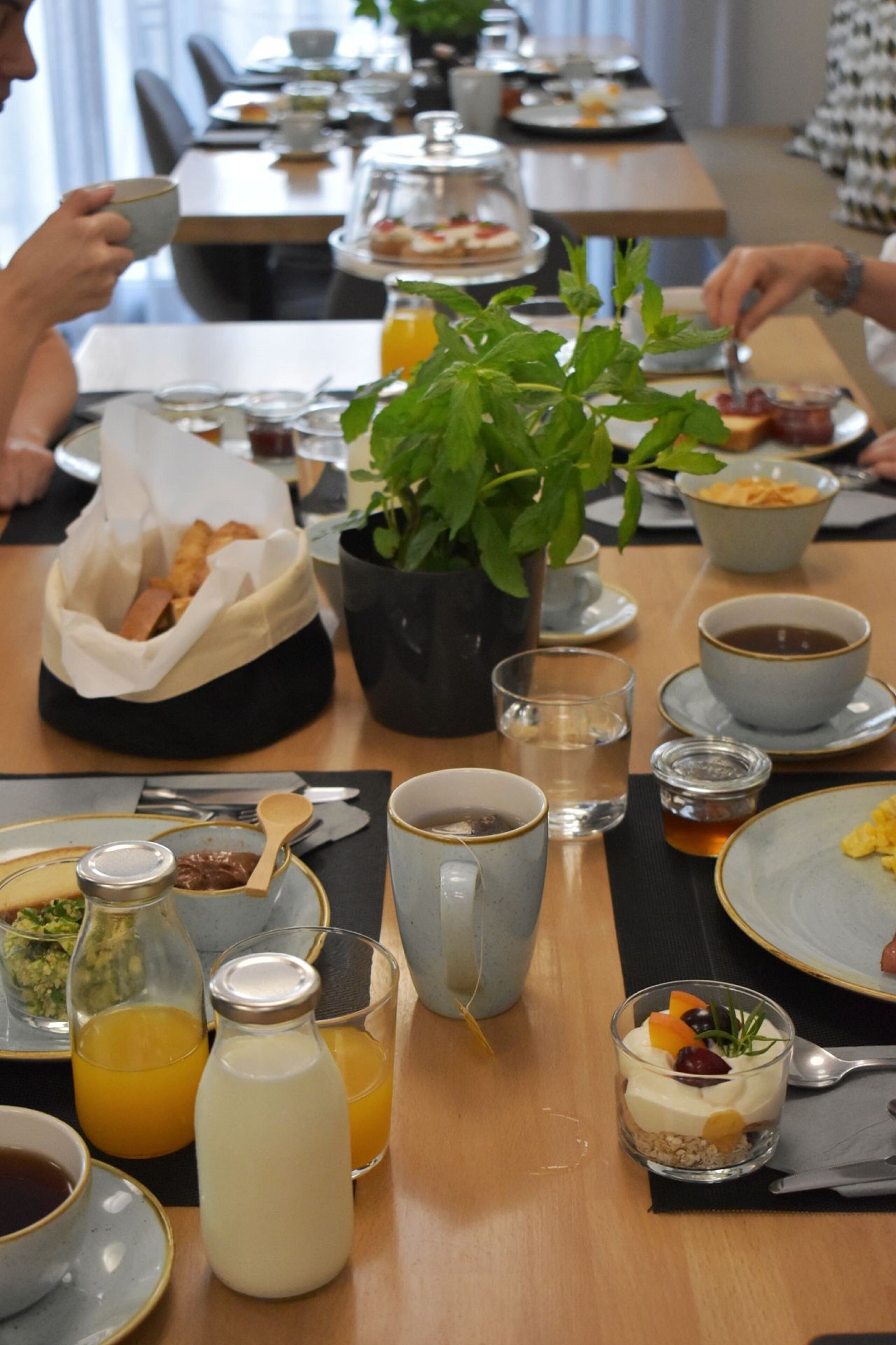 Ein Frühstückstisch mit verschiedenen Speisen, darunter ein Glas Orangensaft, eine Milchflasche und eine kleine Nachspeise.