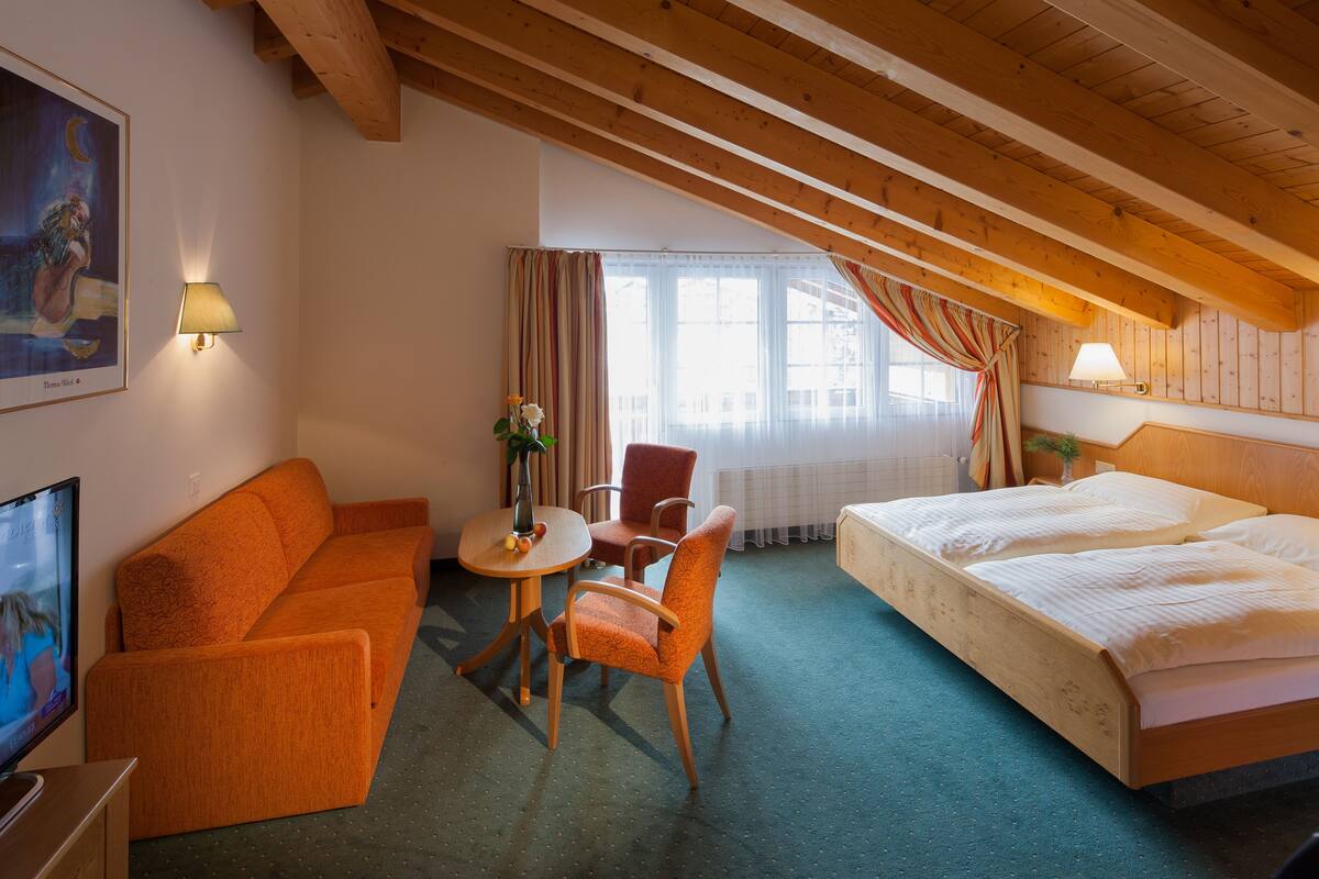 Une chambre d’hôtel avec un plafond en bois, un lit, un canapé, une chaise, une petite table et un téléviseur.