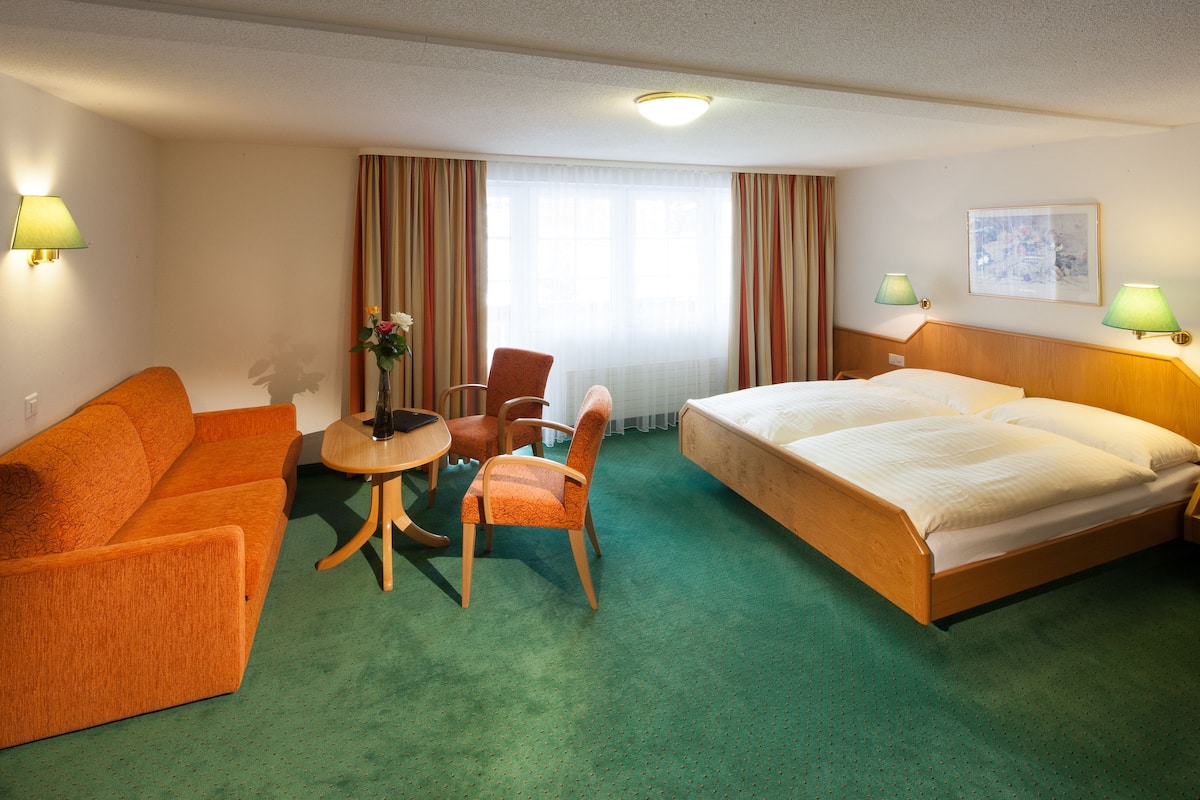 Une chambre d’hôtel avec un lit, un canapé, une chaise, une petite table et une lampe.