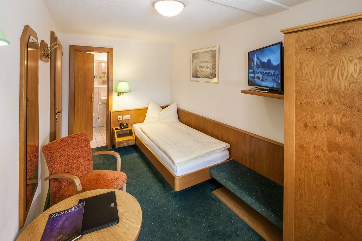 Une chambre d’hôtel avec un lit, une chaise, un bureau, une télévision et une armoire en bois.