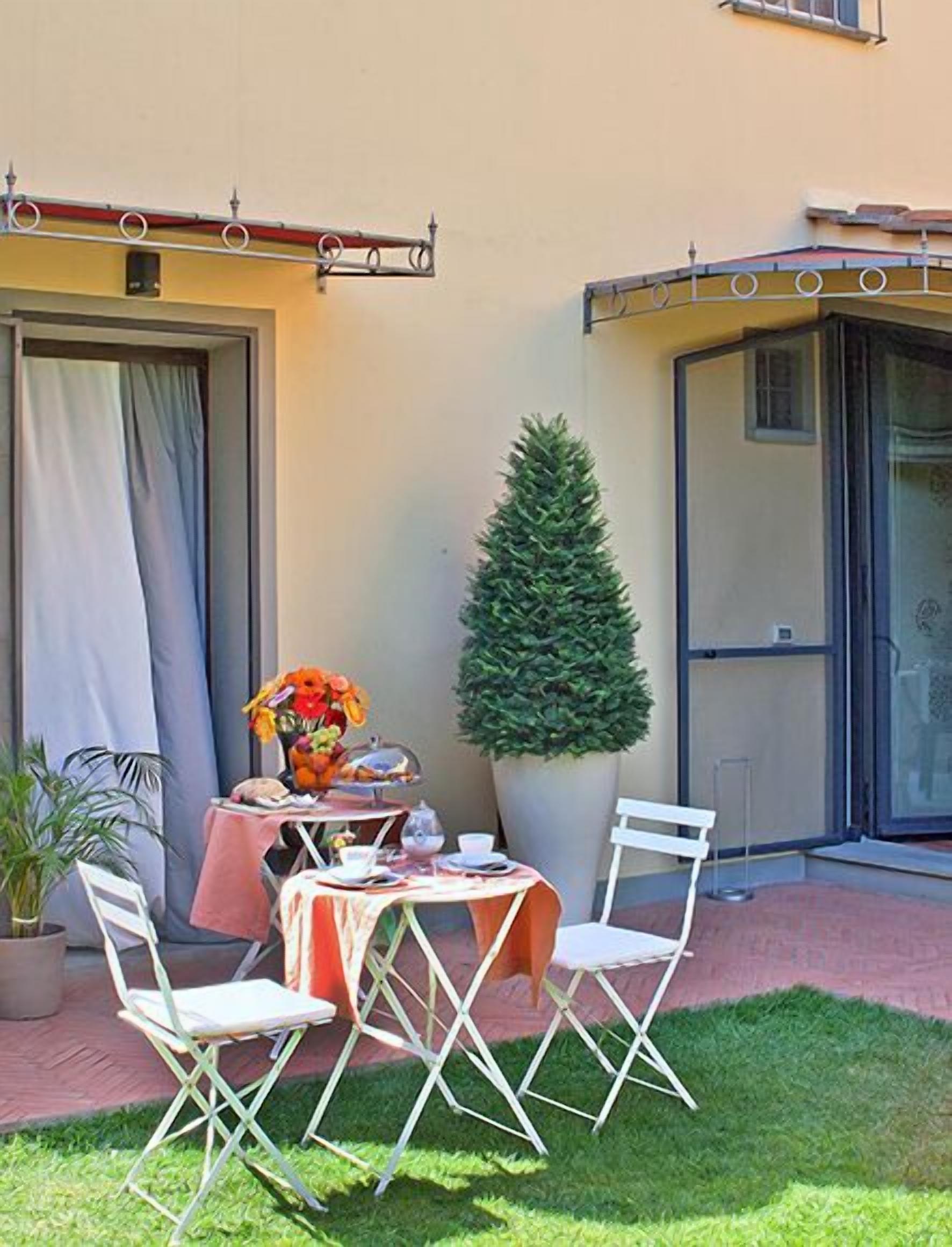 Un patio al aire libre con una mesa para dos, una planta en maceta y un árbol pequeño.