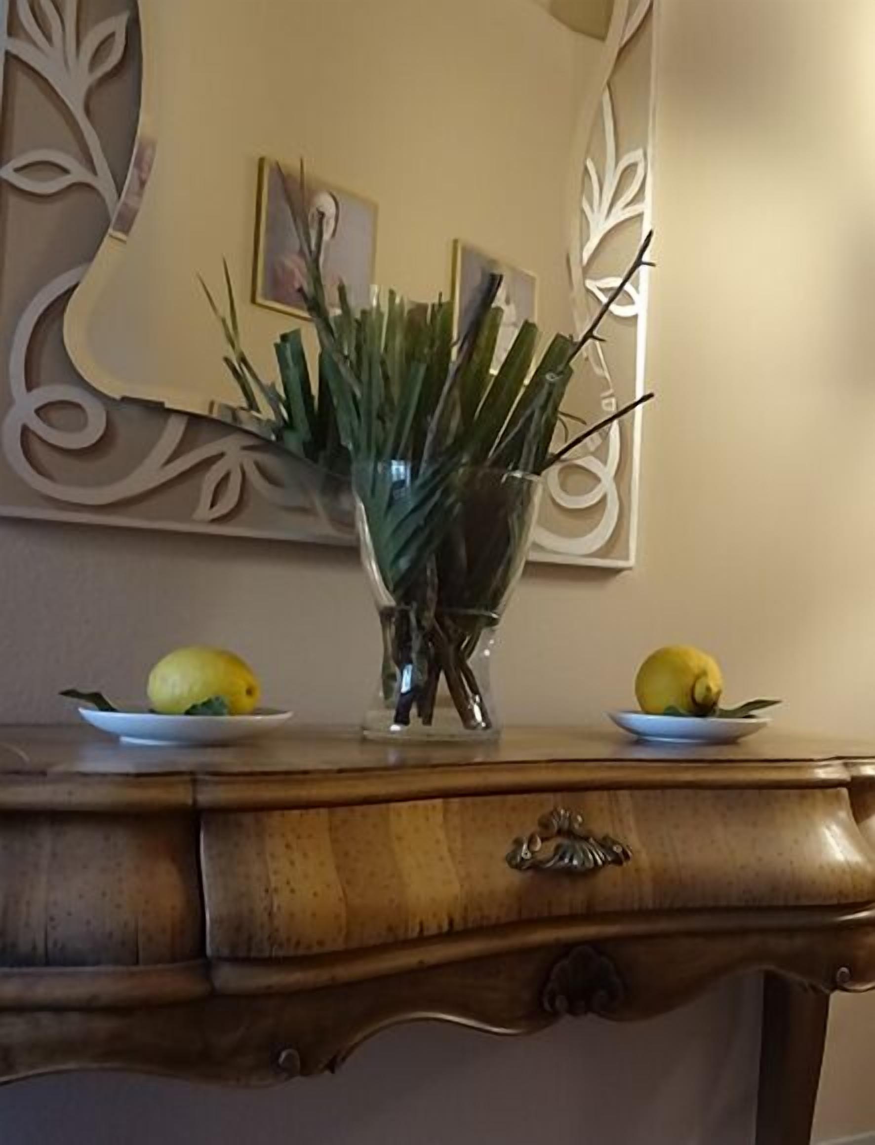 Une table en bois sur laquelle se trouve un vase en verre contenant des feuilles vertes et deux citrons présentés sur des assiettes.