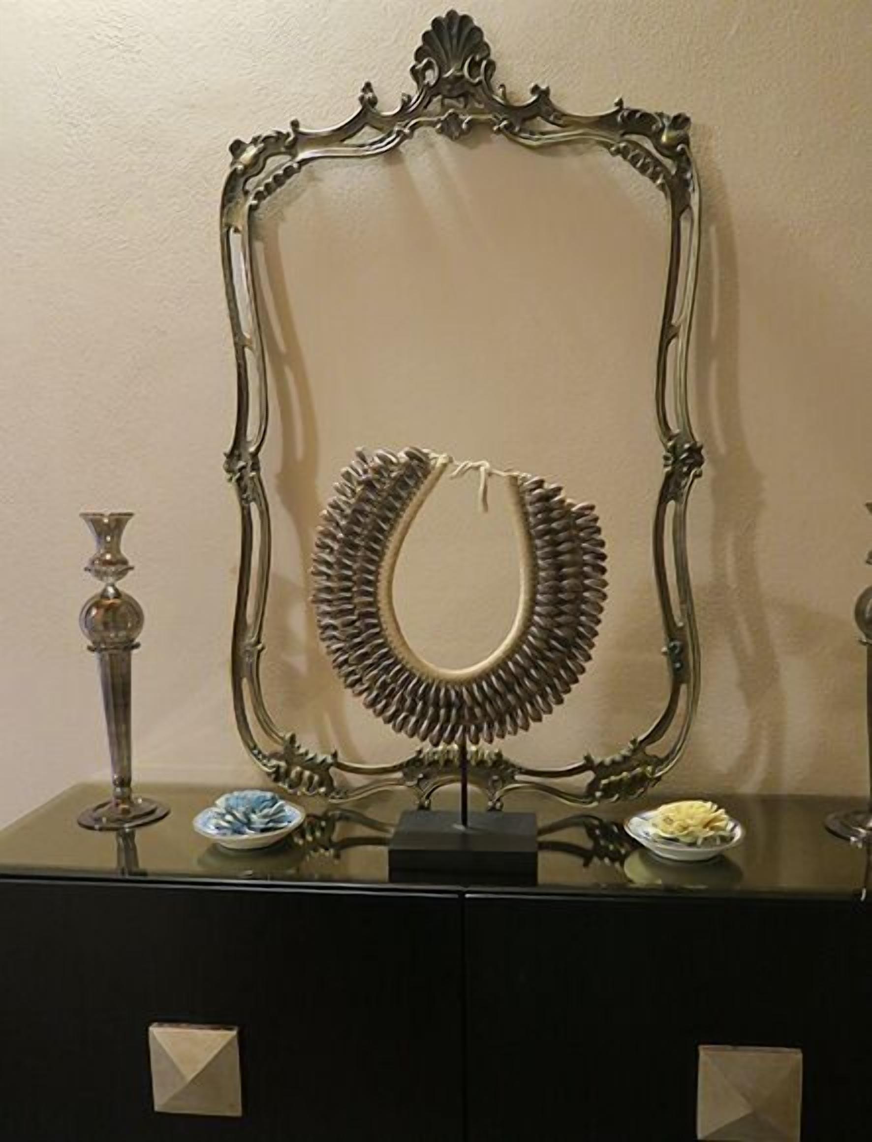 A decorative mirror with an ornate frame, a necklace, and two small vases on a black table.