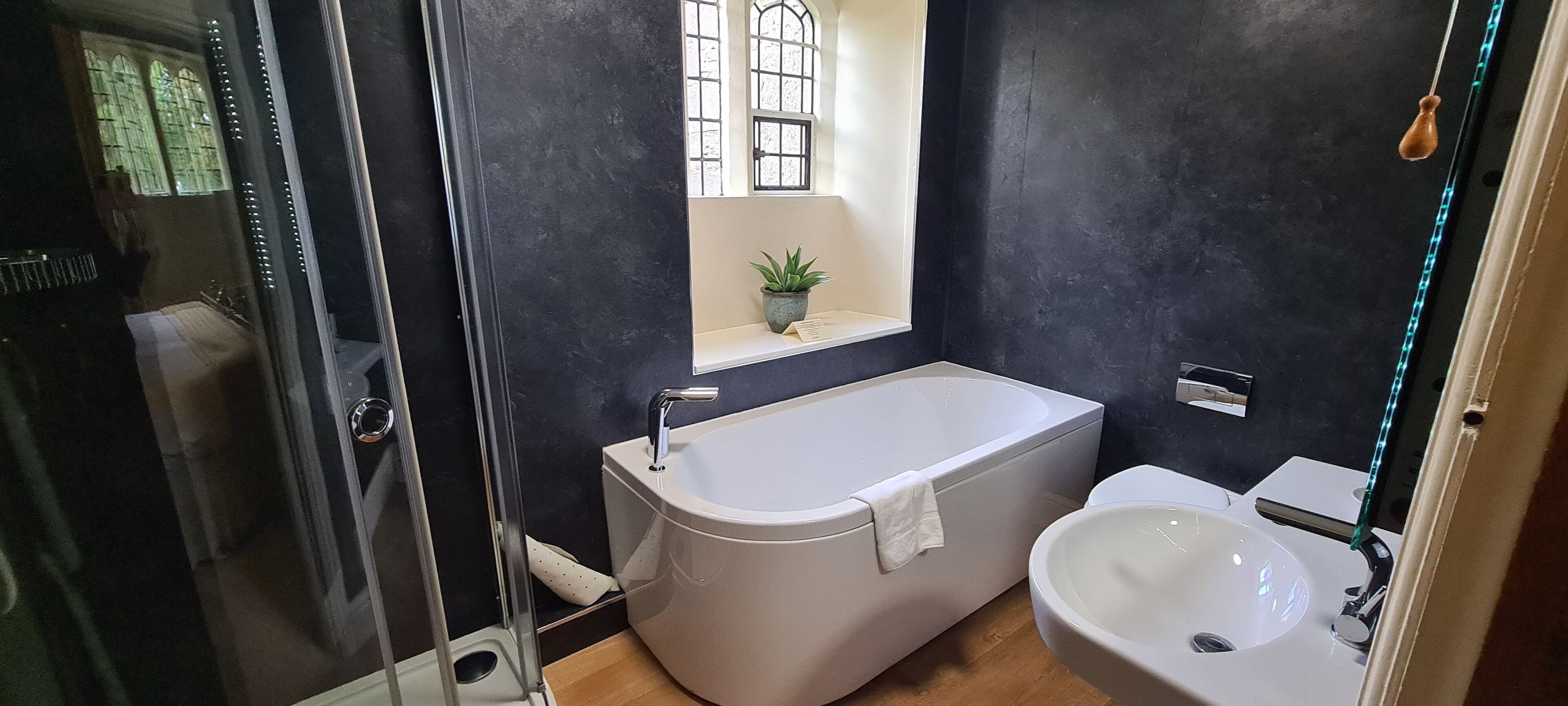 Un baño con bañera, lavabo y una pequeña ventana con una planta.