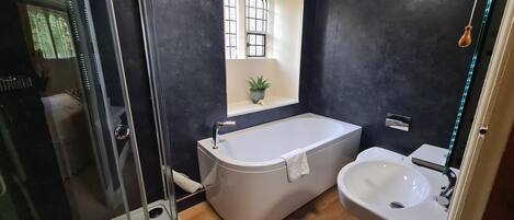 Een badkamer met een badkuip, wastafel en een klein raam met een plant.
