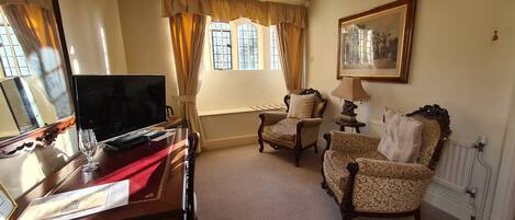 A room with a TV, a desk with a glass, a lamp, and two patterned chairs.