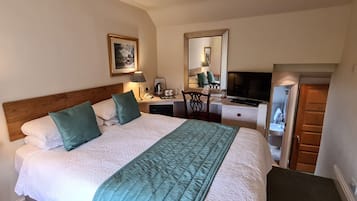 Una habitación de hotel con cama, lámparas de noche, escritorio con computadora, espejo y armario.