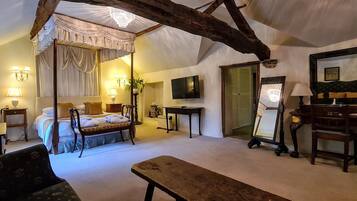 A bedroom with a four-poster bed, a desk, a chair, a bench, a television, and a mirror.