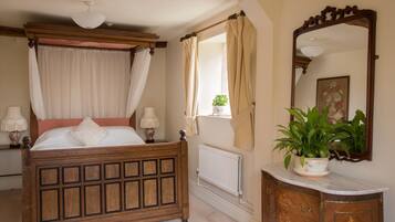 A bedroom with a four-poster bed, a radiator, a mirror, and a potted plant.