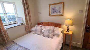 A neatly made bed with plaid bedding, a bedside lamp, a framed picture on the wall, and a window with curtains.