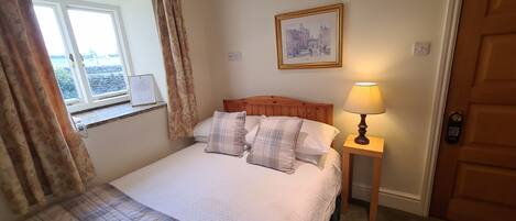 A neatly made bed with plaid bedding, a bedside lamp, a framed picture on the wall, and a window with curtains.