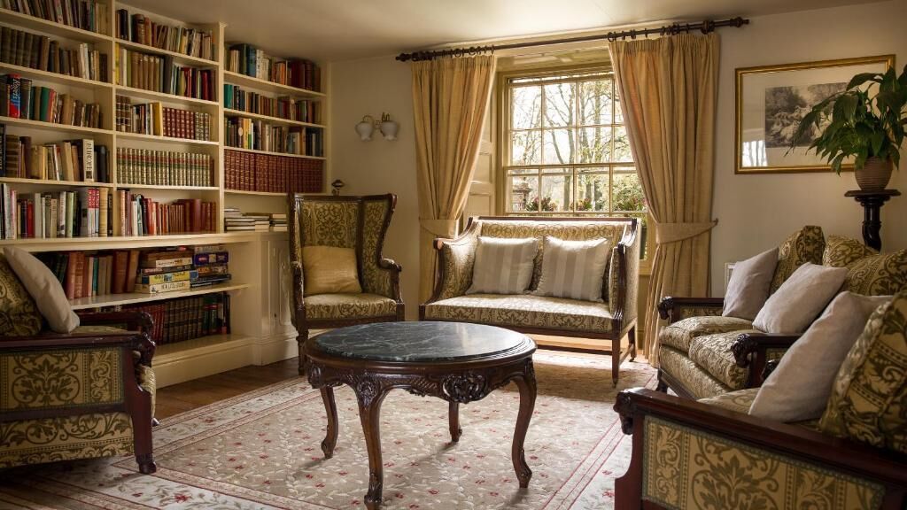 Une bibliothèque avec des étagères, une table ronde et deux fauteuils rembourrés.