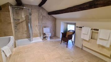 A bathroom with a glass-enclosed shower, a white bathtub, a toilet, and a wicker chair.