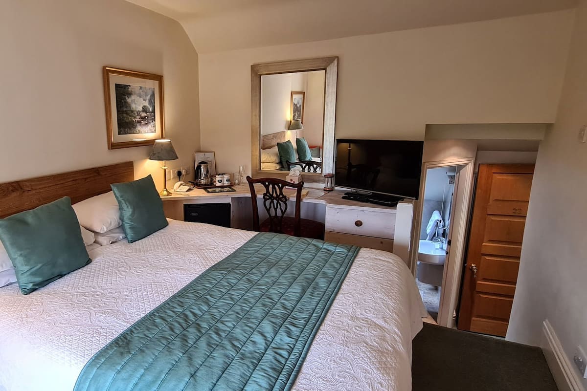 A hotel room with a bed, bedside lamps, a desk with a computer, a mirror, and a wardrobe.