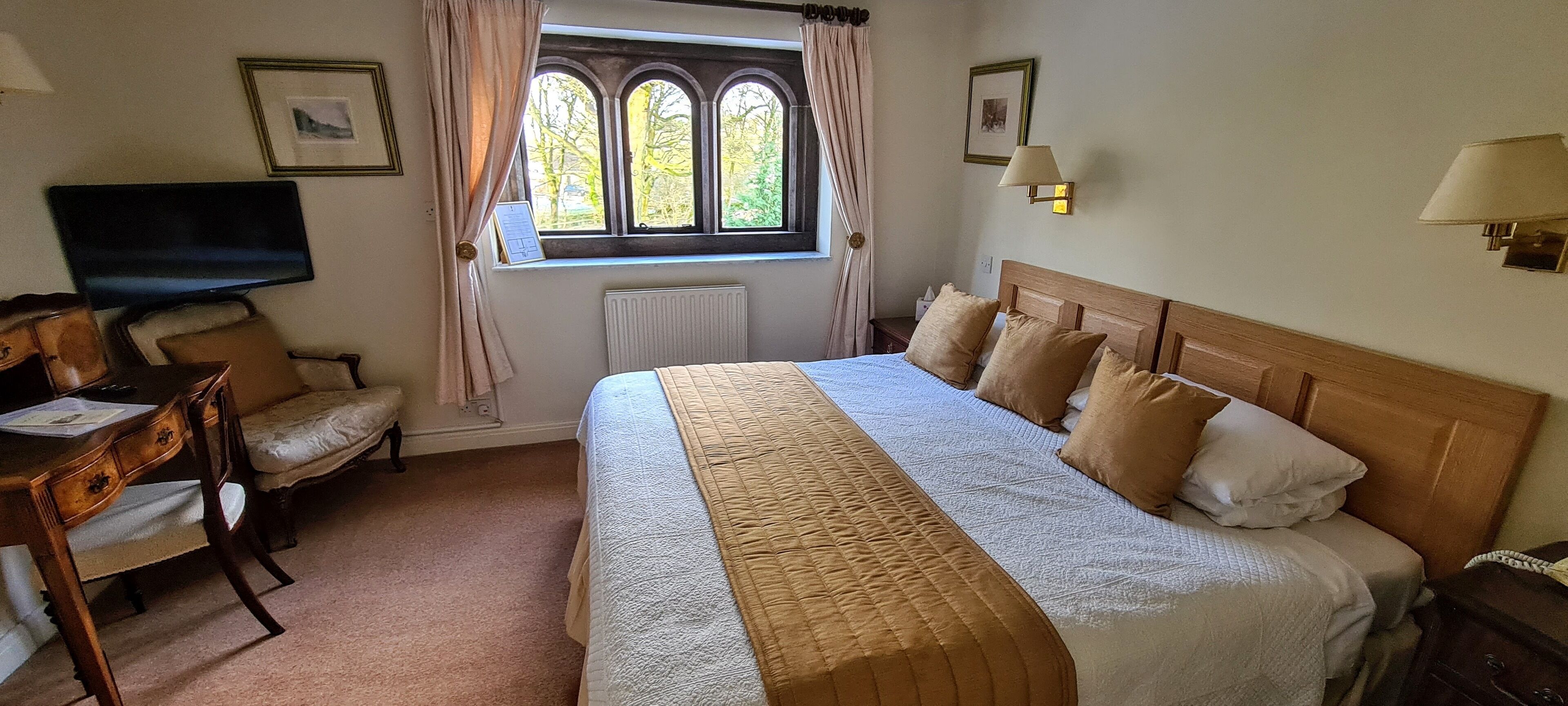 A hotel room with a large bed, a desk with a chair, a television, and a window with curtains.
