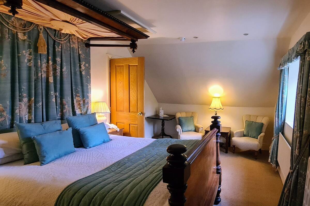A bedroom with a large bed, two chairs, a table, and a door.