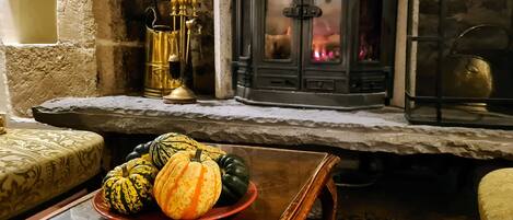 A cozy living room with a stone fireplace, a wooden table with a plate of gourds, and a patterned sofa.