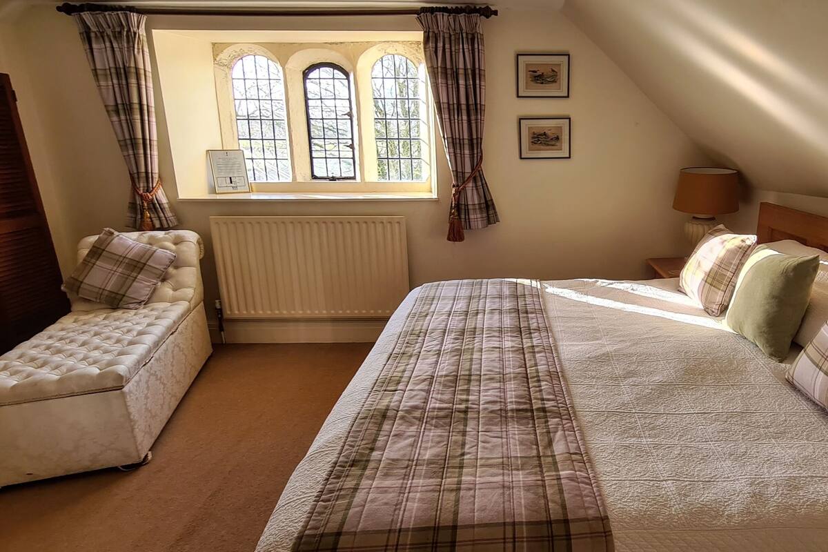 A bedroom with a bed, bench, window, radiator, lamp, and framed pictures.