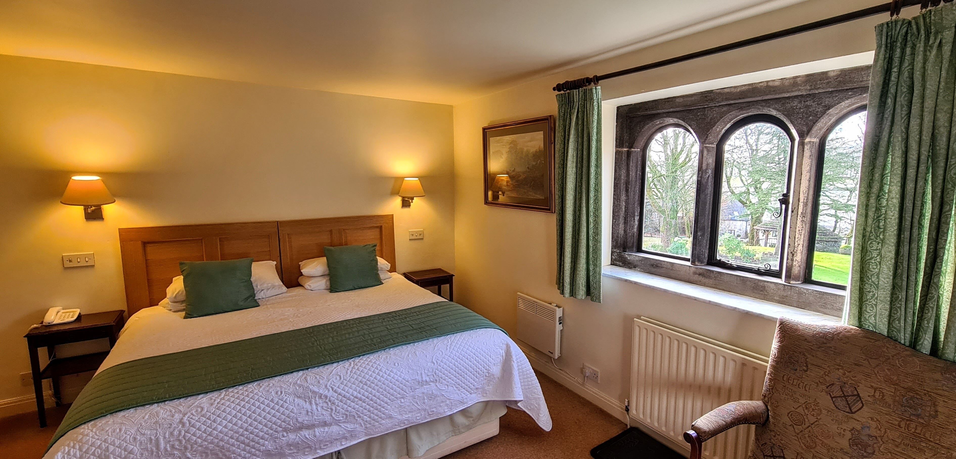 A neatly arranged bedroom with a bed, bedside lamps, a radiator, and a window with curtains.