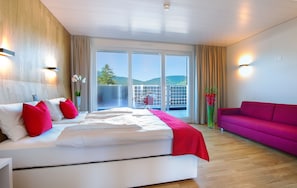 A modern hotel room with a large bed, a balcony with a view, a bright pink sofa, and a wooden wall. - Hotel Rhy (Oberriet)