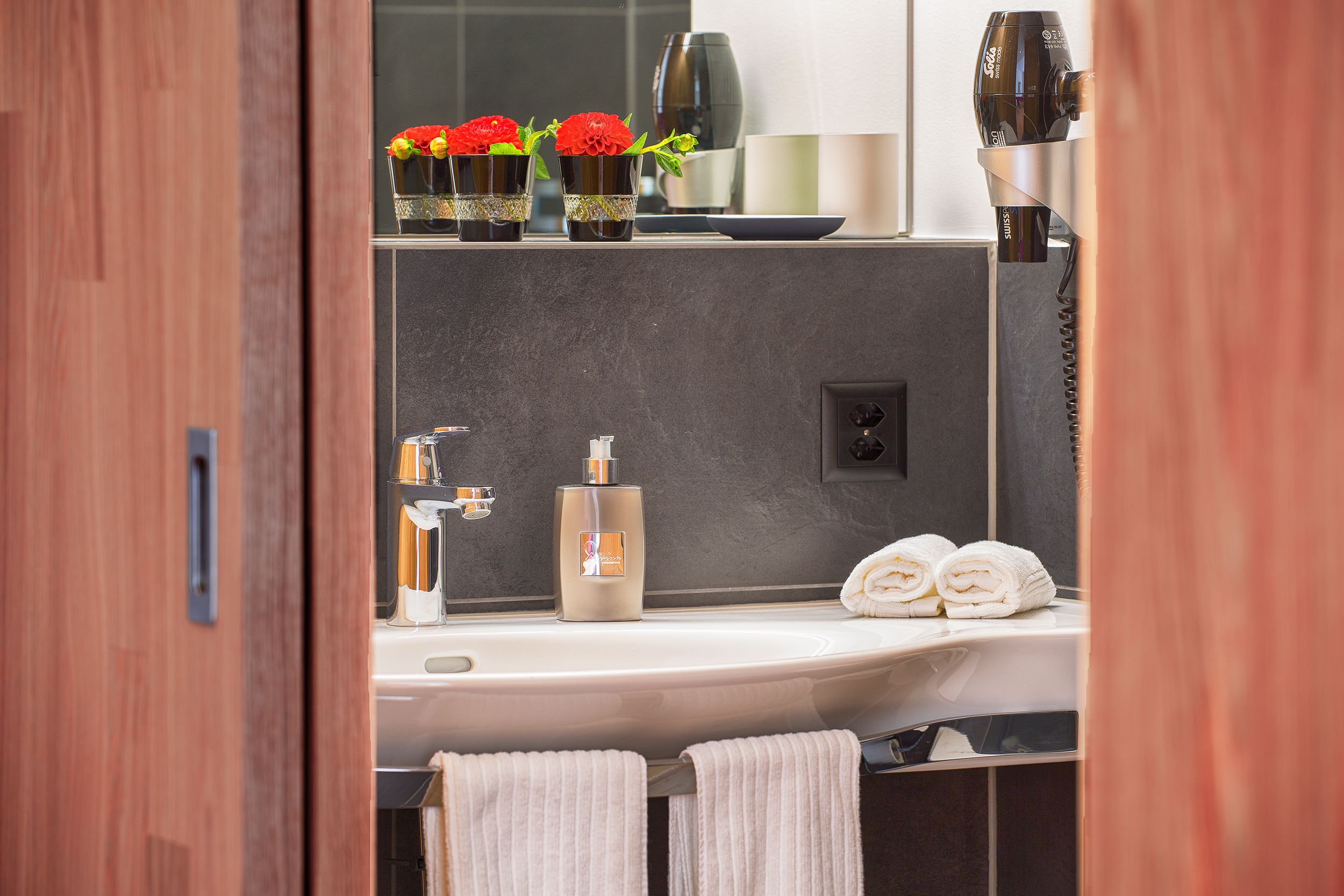 A bathroom with a modern sink, a hairdryer, and two towels.