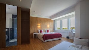 A modern bedroom with a large bed, bedside tables, a walk-in closet, and a bathroom with a glass shower. - Hotel Rhy (Oberriet)