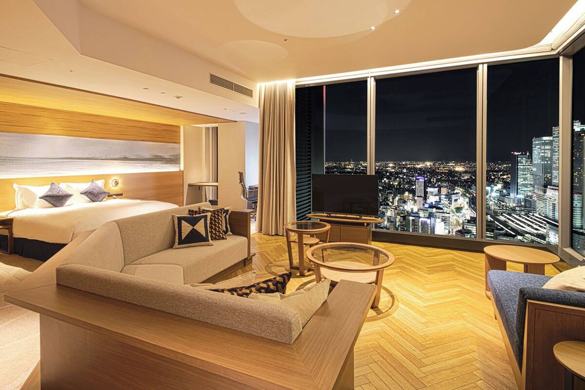 A modern hotel room with a large bed, a sofa, a TV, and a city view.