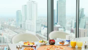 A breakfast table with plates of food, a pizza, and glasses of orange juice, set against a cityscape view.