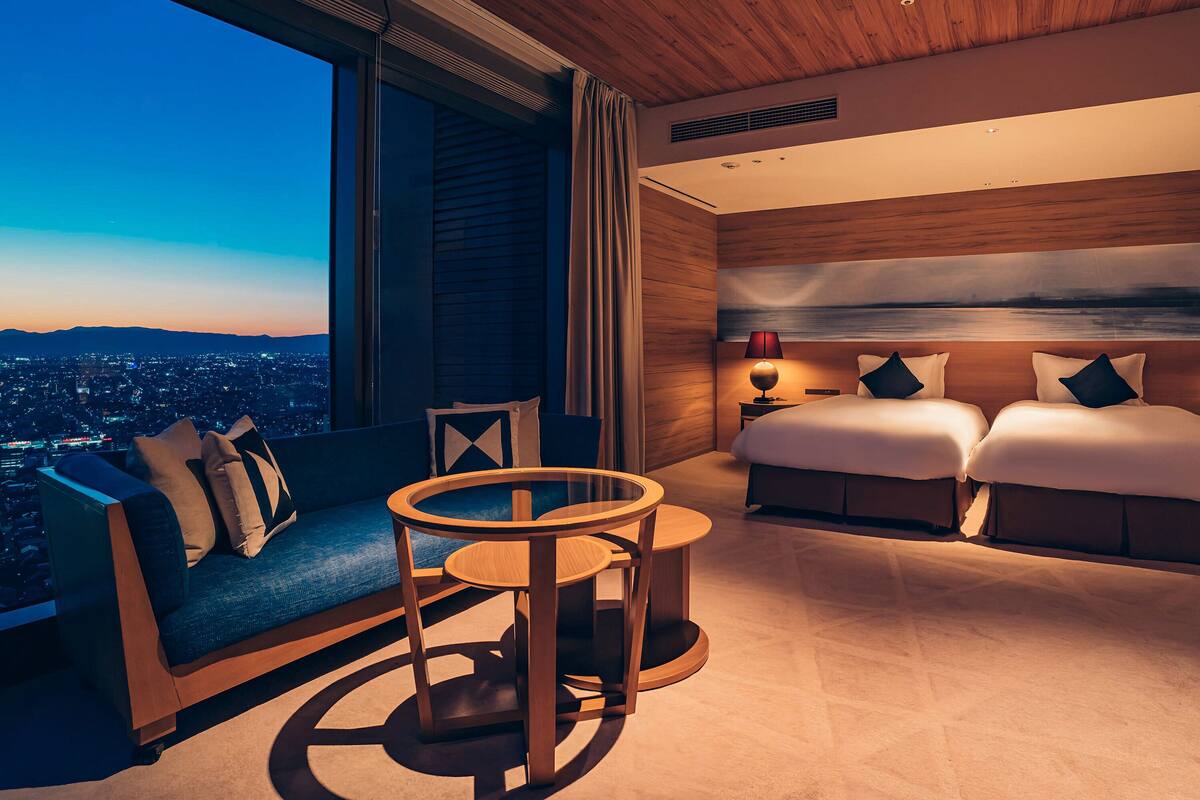 A modern hotel room with a large window, a sofa, a round table, and a bed.