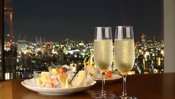 A table with two champagne flutes and a plate of appetizers against a cityscape view.