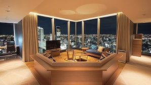 Un salon moderne avec un canapé aux lignes courbes, une table basse et un téléviseur. De grandes fenêtres offrent une vue sur la ville.