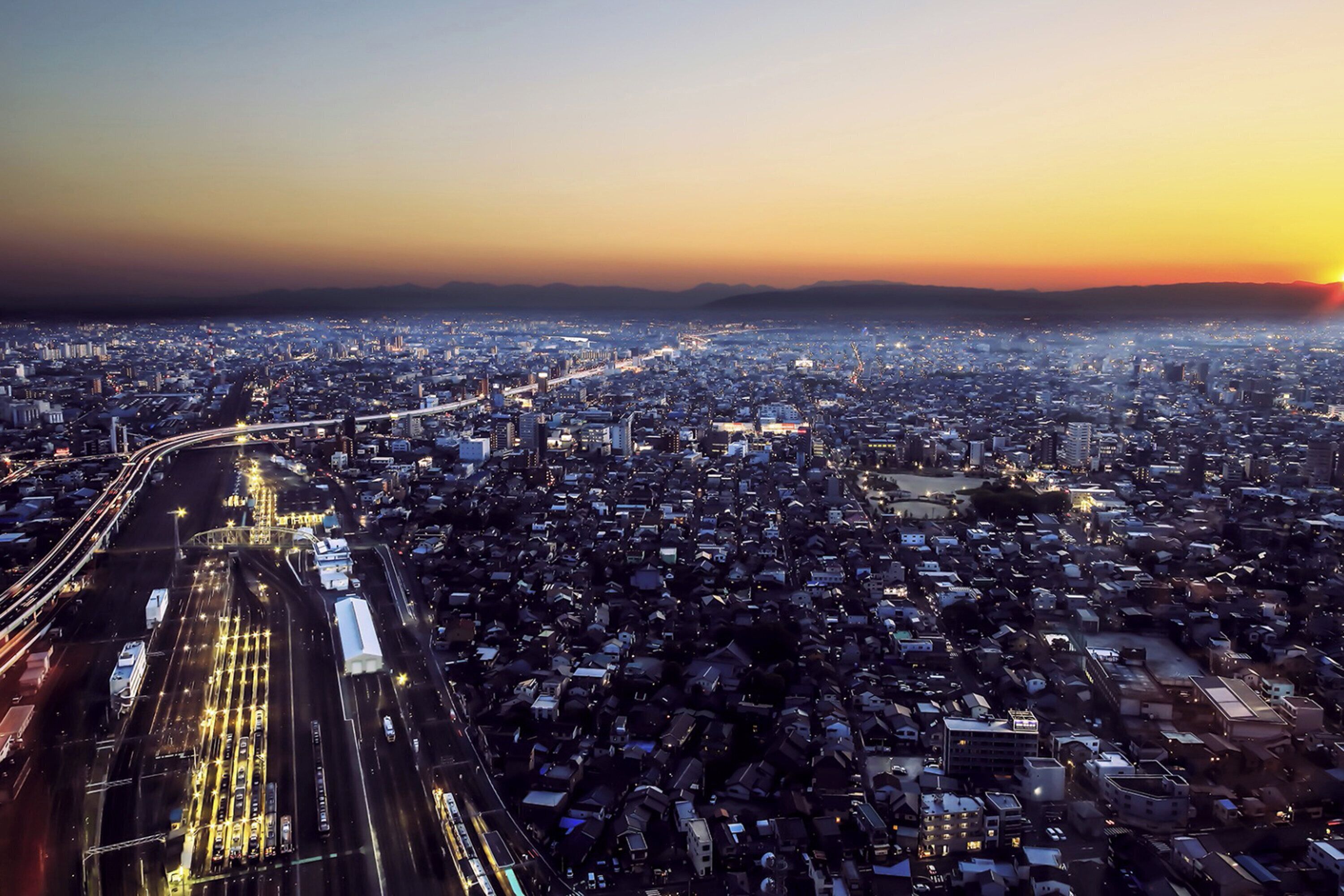 An aerial view of a cityscape at dusk with illuminated streets and buildings.