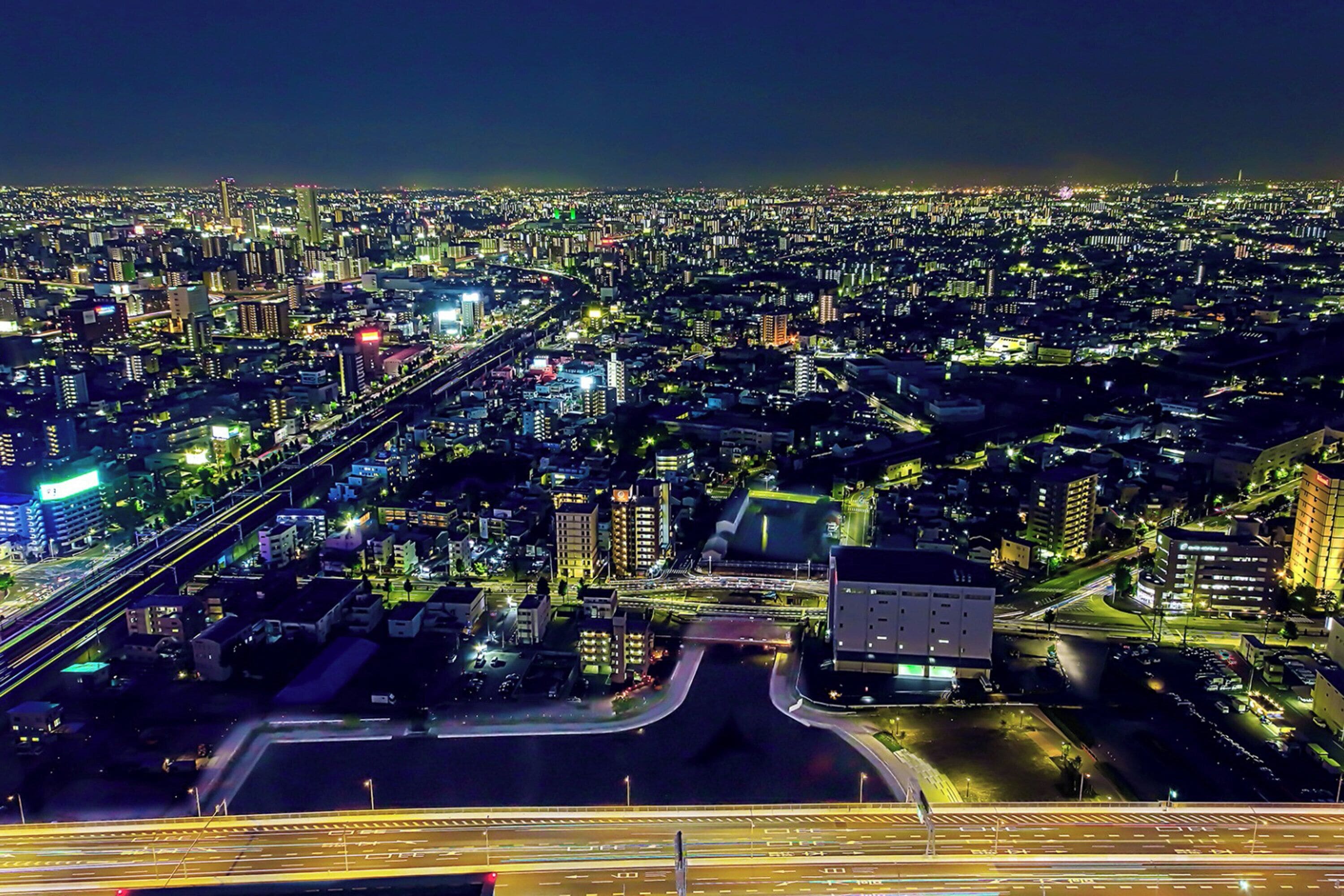 Ein Luftbild einer beleuchteten Stadtlandschaft bei Nacht mit Gebäuden, Straßen und Autobahnen.