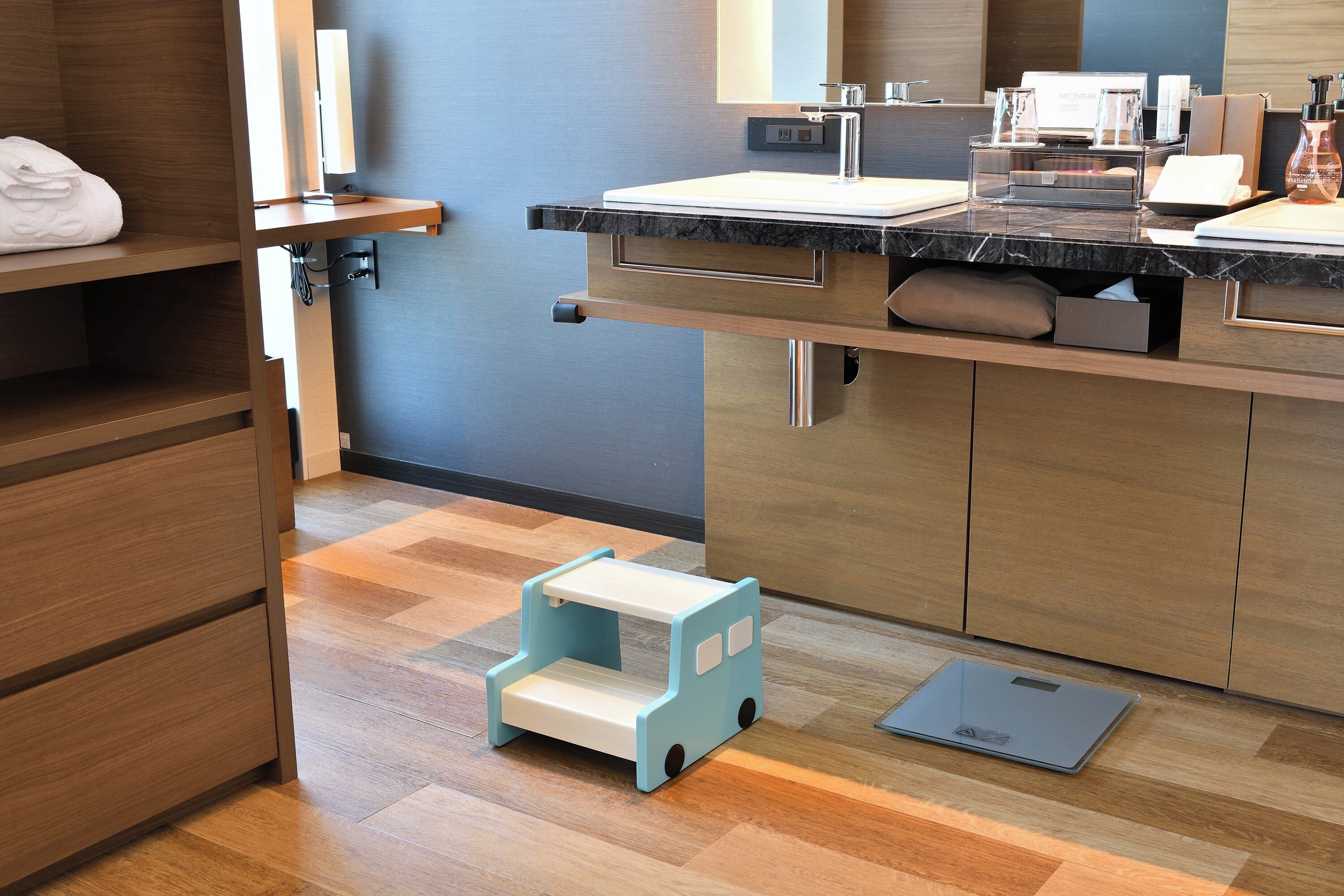 Een moderne badkamer met een marmeren wastafel, een klein opstapkrukje en een digitale weegschaal.