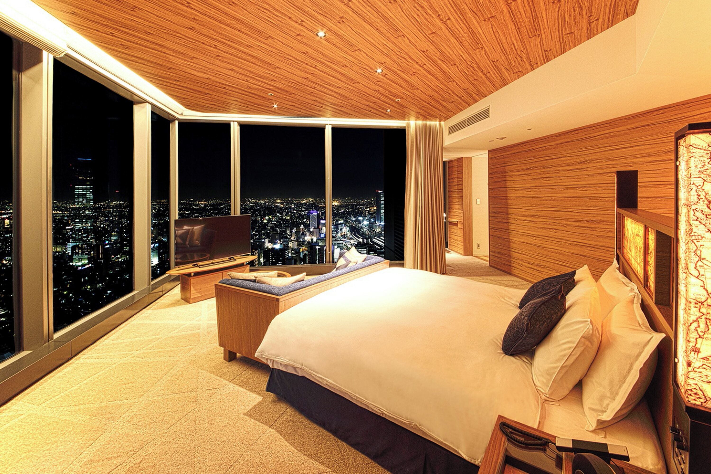A modern hotel room with a large bed, a TV, and a city view.