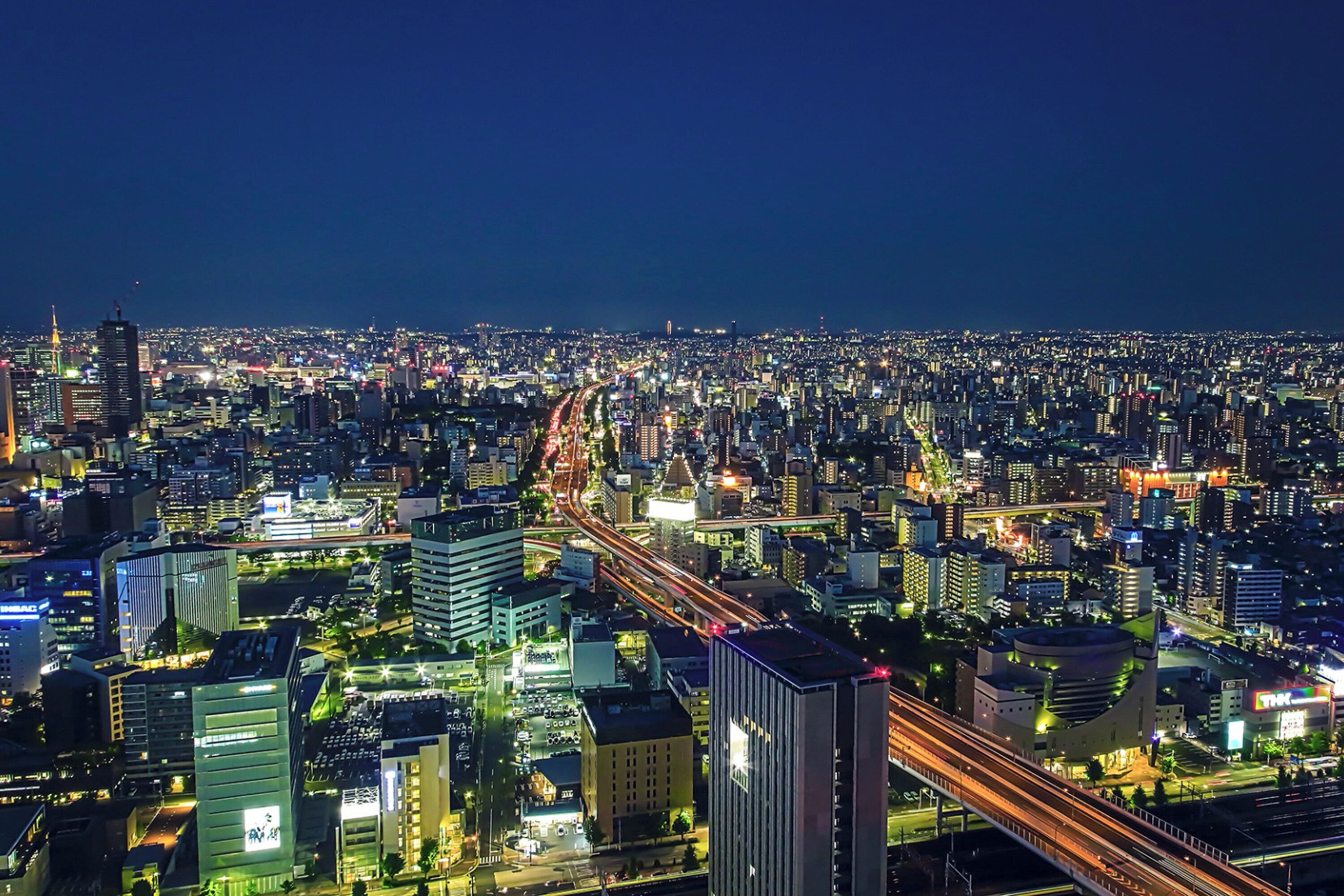 A nighttime cityscape with illuminated buildings and a busy highway.