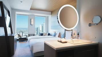 A modern hotel room with a large bed, a bedside table with a mirror, a desk, and a view of the city through large windows.