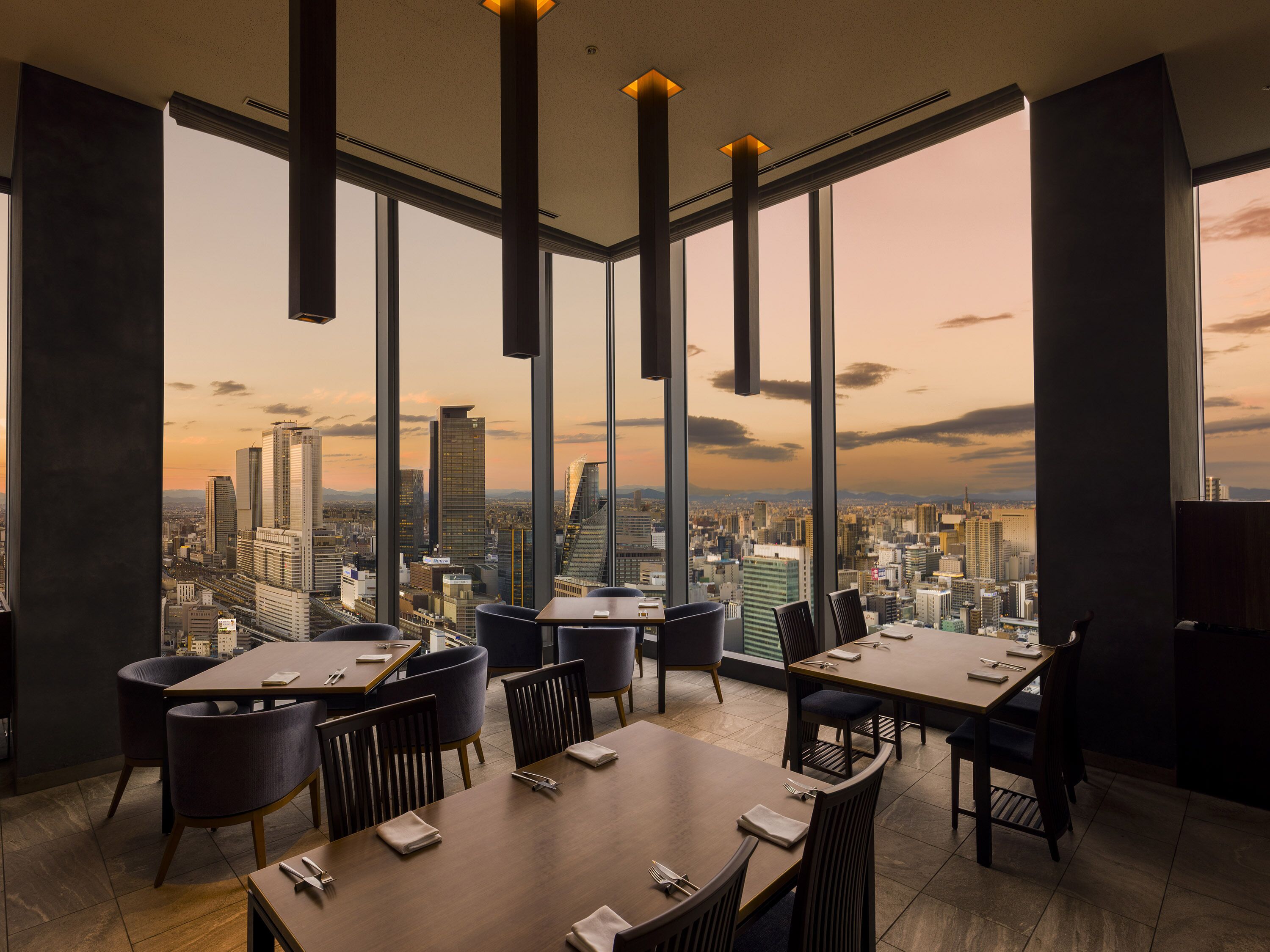 A modern dining area with high ceilings and large windows offering a cityscape view.
