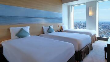 Habitación de hotel con dos camas, un ventanal con vistas a la ciudad y un cuadro en la pared.