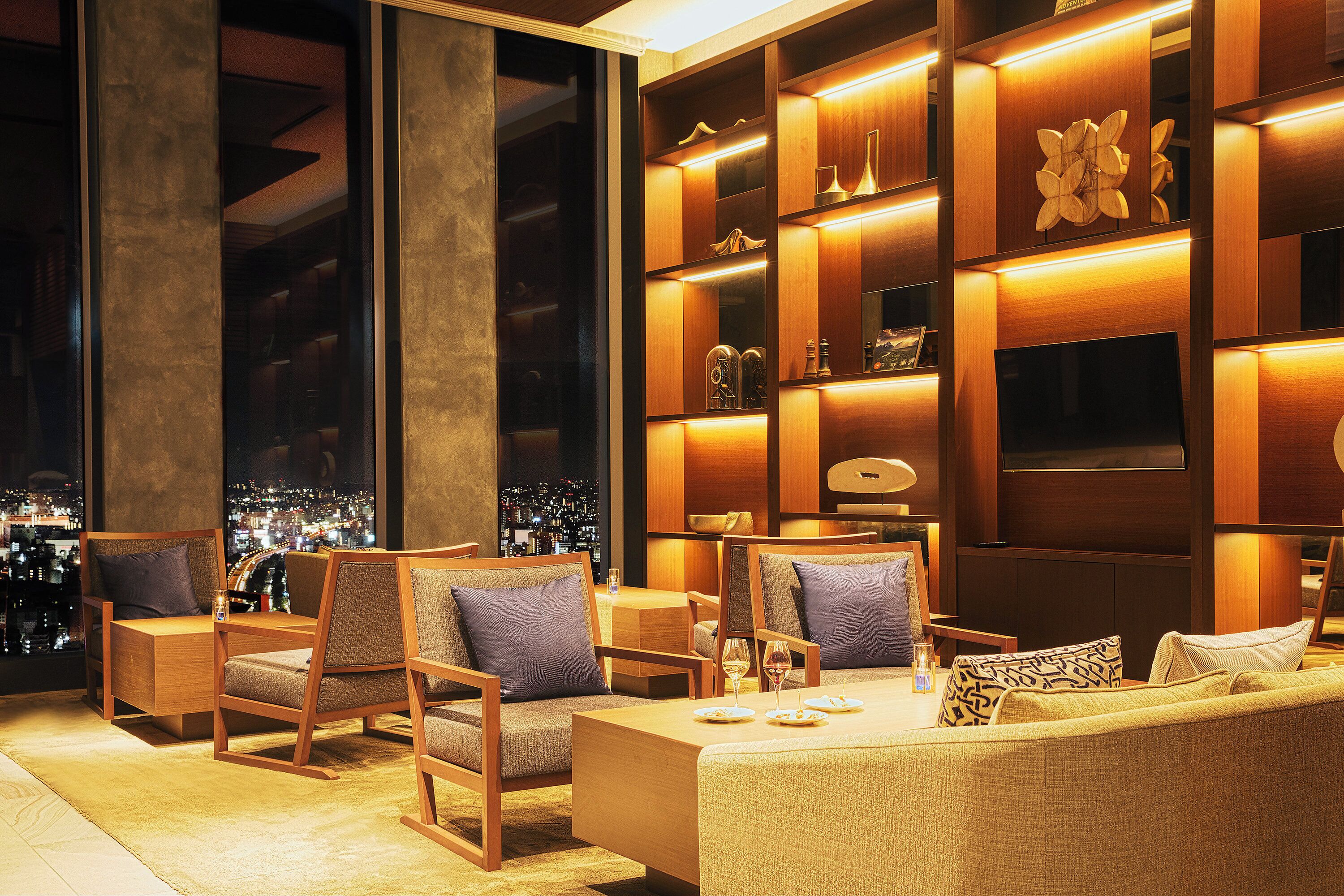 A modern hotel lobby with a large window offering a city view, wooden furniture, and a well-lit interior.