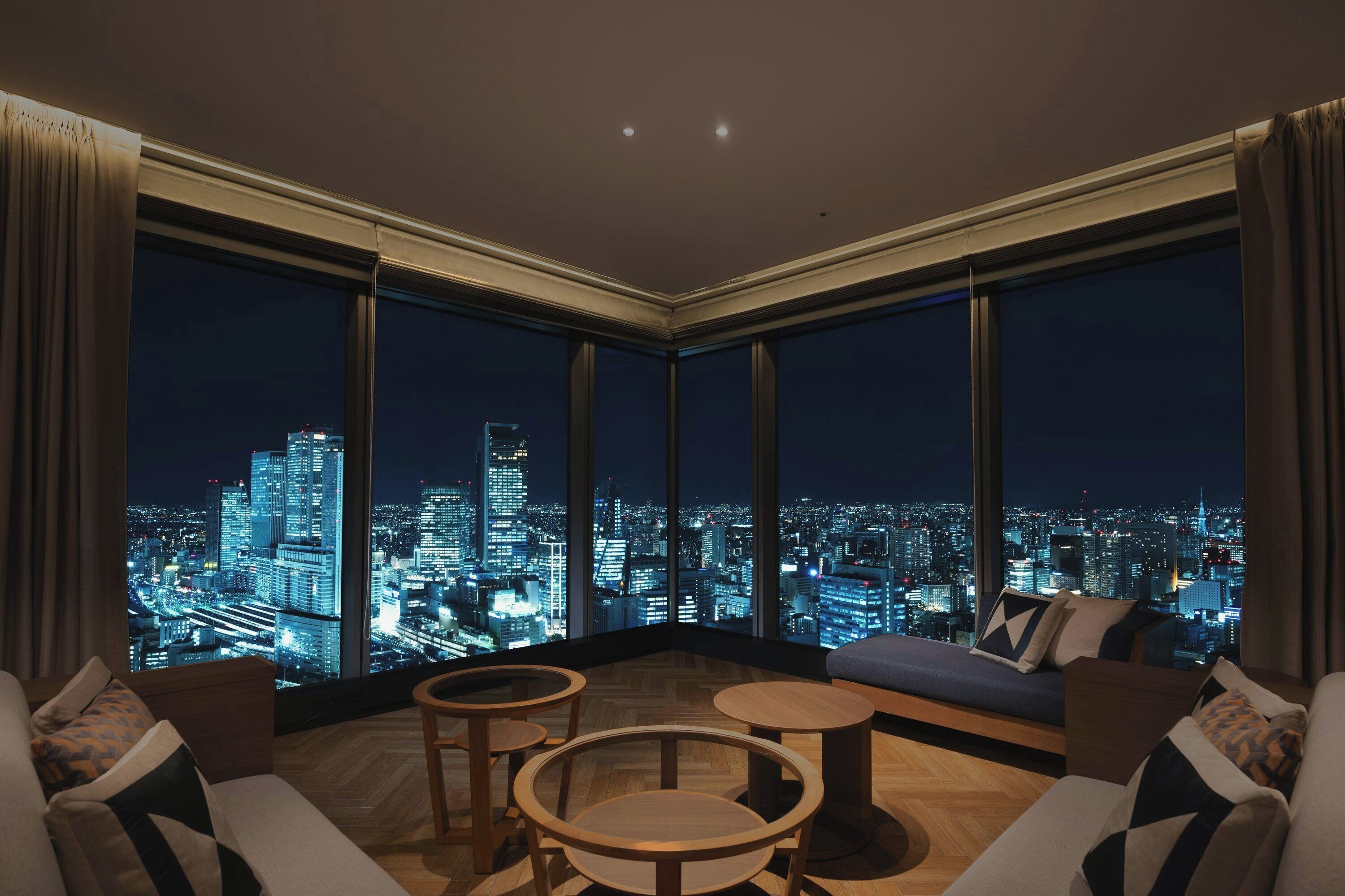 A high-rise room with a city view, a sofa, two small tables, and a large window.