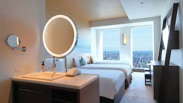 Una habitación de hotel moderna con una cama grande, una mesita de noche con espejo, un escritorio y vistas a la ciudad.