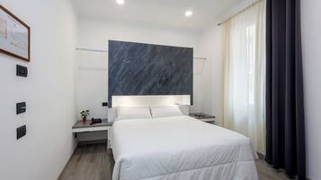 A modern hotel room with a large bed, a bedside table with a lamp, a nightstand, and a wall-mounted artwork.