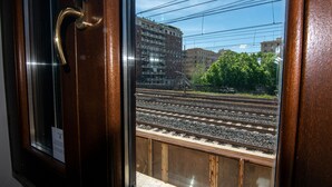 Uitzicht door een raam met houten frame en een messing handgreep, op spoorwegen en gebouwen in de verte.