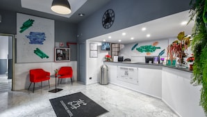 Een moderne hotel receptie met een marmeren vloer, rode stoelen, een receptiebalie en een klok aan de muur.
