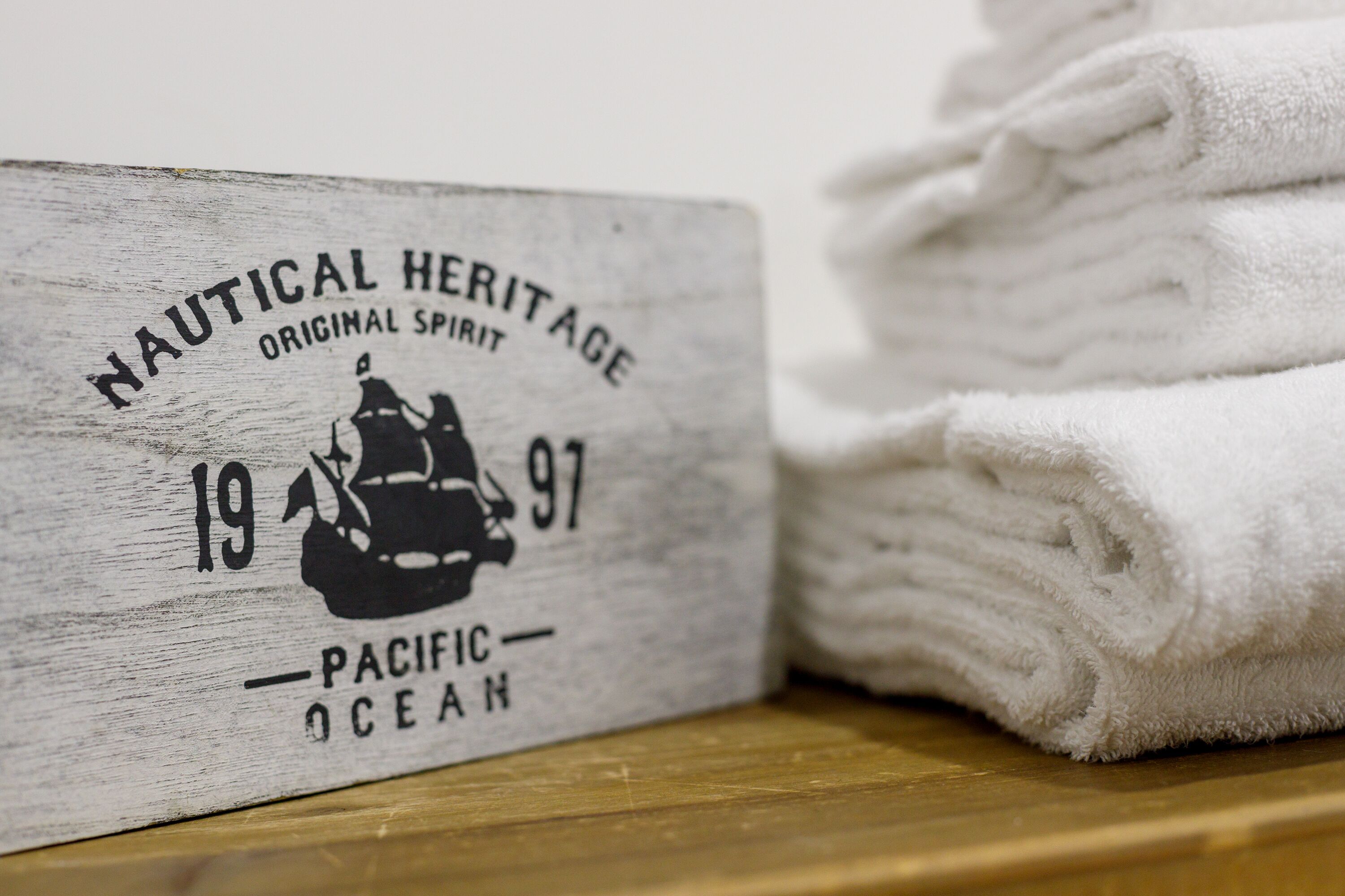 A wooden sign with text and a ship illustration, next to a stack of white towels.