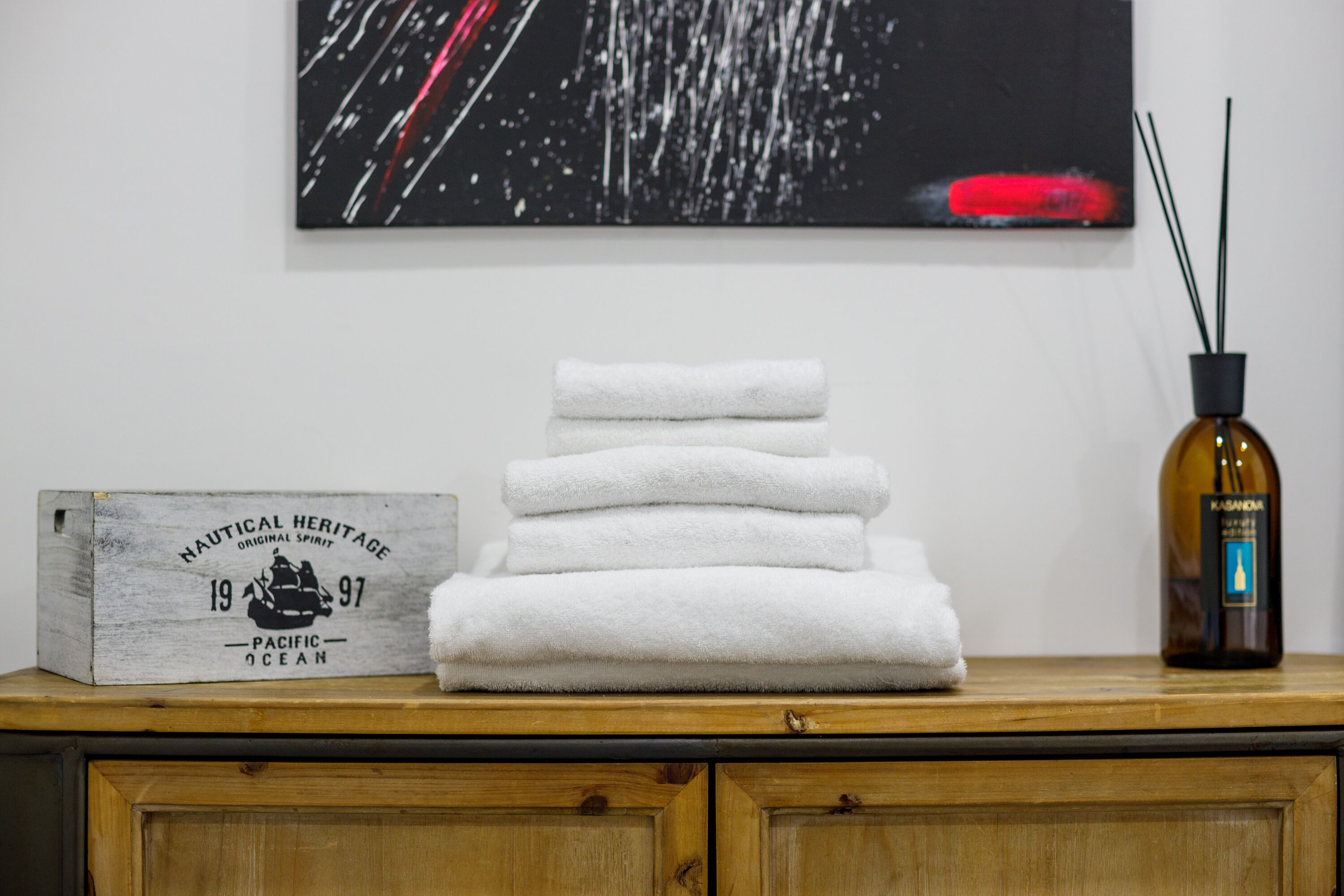 A stack of white towels on a wooden surface, a wooden box with text, and a bottle with a label.
