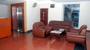 A lobby with a reception desk, a wall-mounted clock, a large window, and a seating area with leather sofas and a coffee table.
