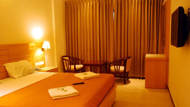 Una habitación de hotel con una cama, dos sillas, una mesita de noche, una lámpara y un televisor.