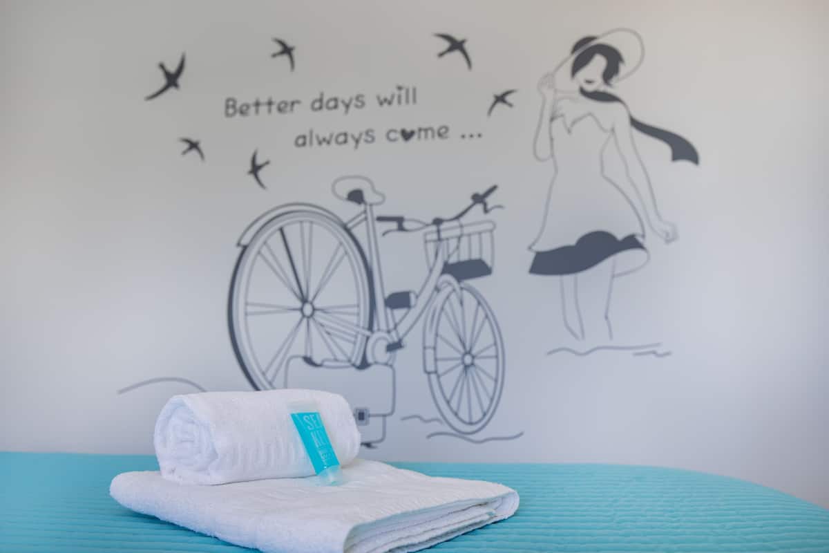 A towel on a bed with a wall art featuring a bicycle and a woman, and a text saying "Better days will always come...".